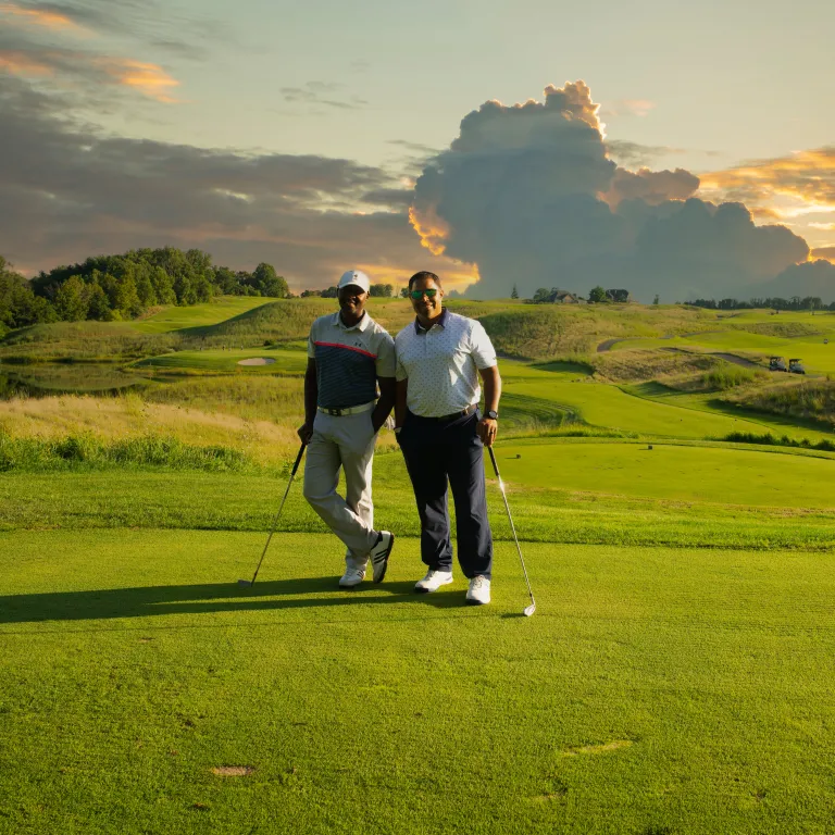 Two golfers stand on Ballyowen Golf Course with sunset behind them. 