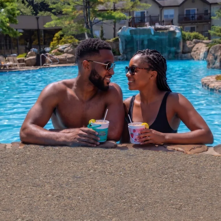 Couple on side of pool drinking rum buckets.