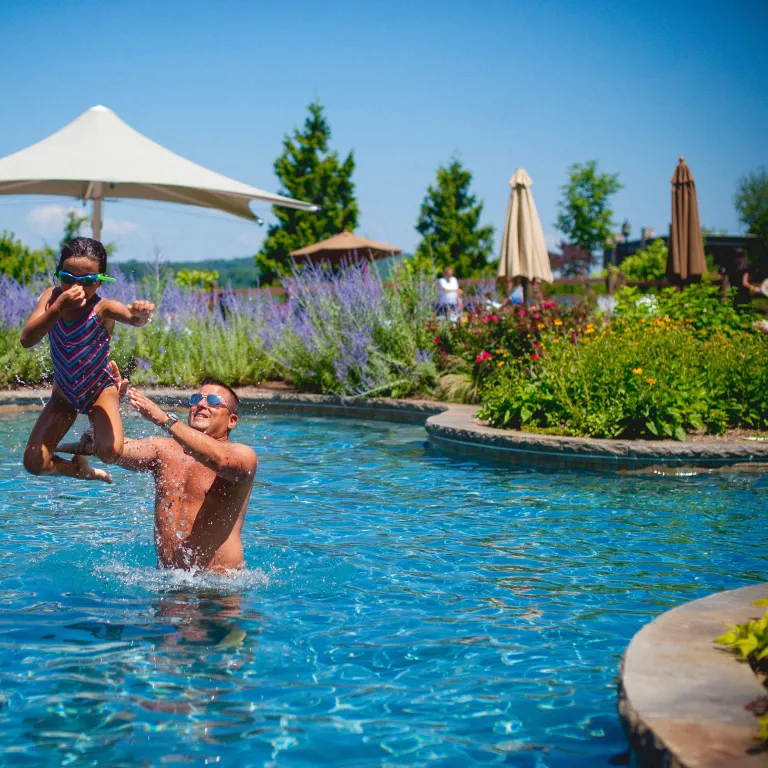 Young girl midair as her father throws her in pool.
