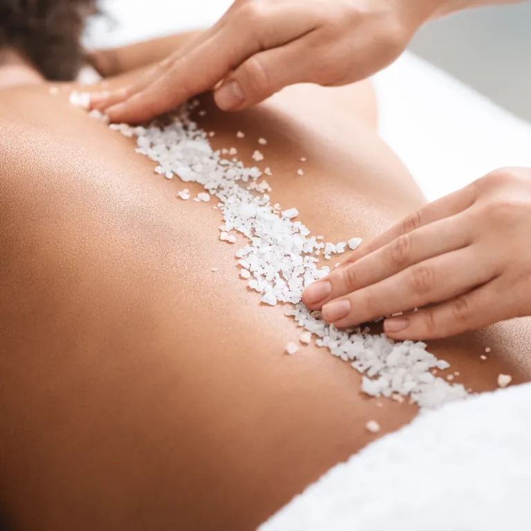 Salt scrub down woman's back during spa treamtment.