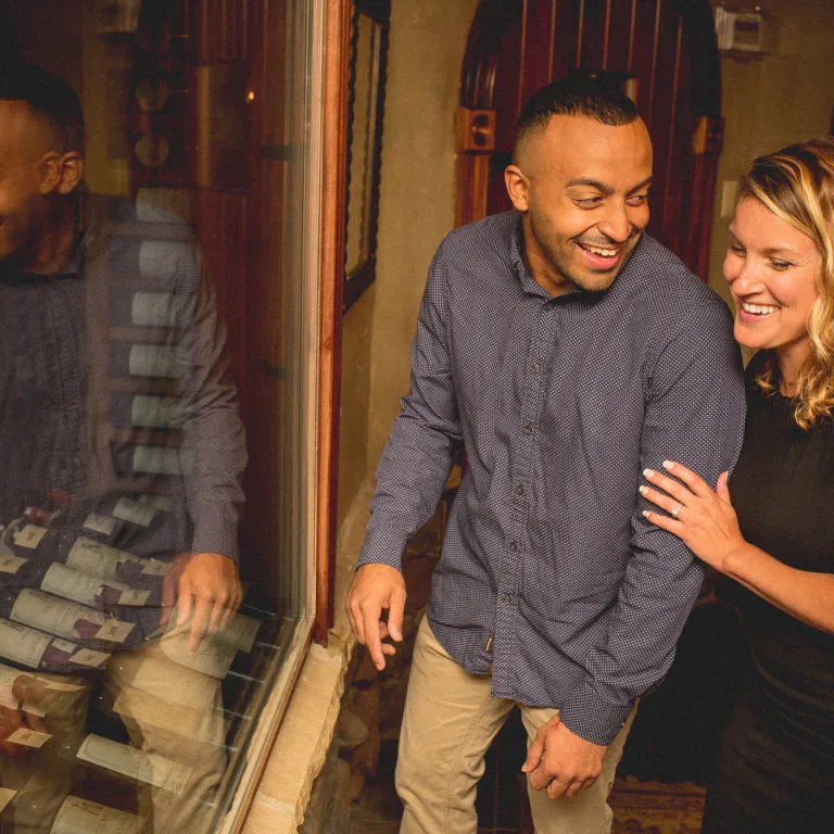 Man and woman on wine cellar tour looking through glass at wine bottles.