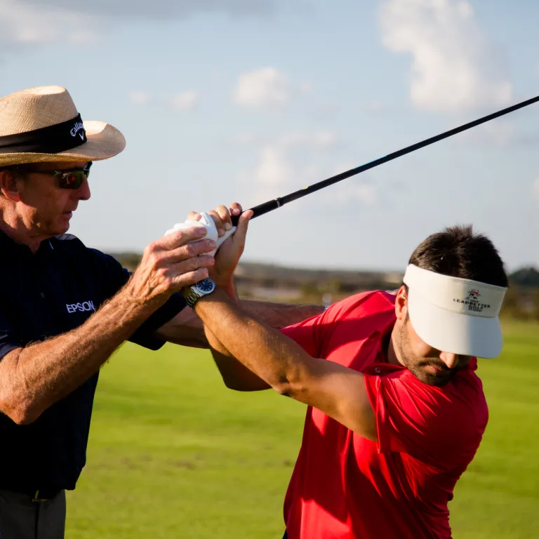 Golf instructor giving lessons to man in red shirt