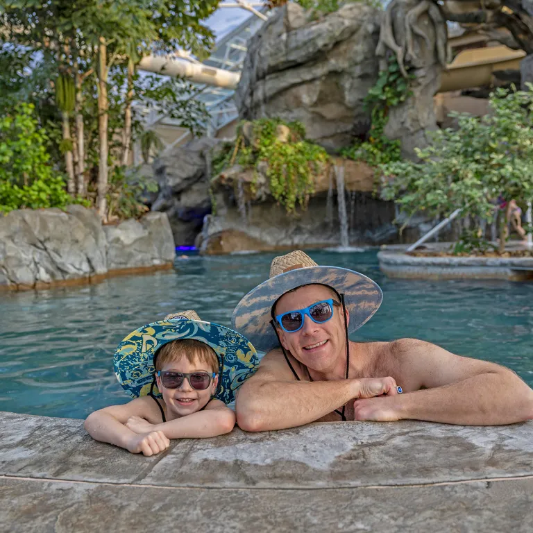 Father and son wearing matching hats and sunglasses in Biosphere pool.