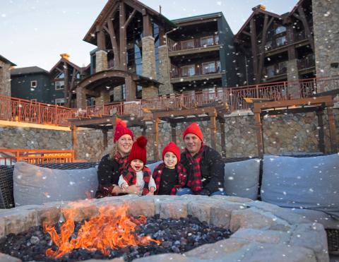 Family of four sits around firepit as it snows around them on Fire & Water Terrace