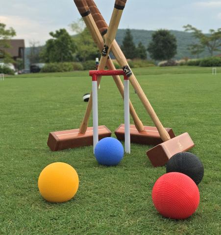 4 croquet balls on the grass and 3 croquet mallets leaning against a wicket
