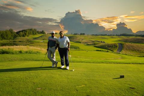 Two golfers stand on Ballyowen Golf Course with sunset behind them. 
