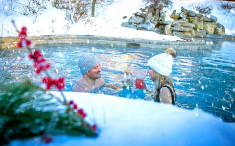 Couple drinks cocktails in outdoor snow pool.
