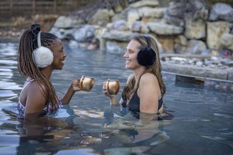 Two women wearing earmuffs in outdoor pool. 