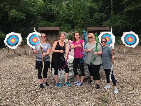 Five girlfriends holding bows at archery range. 