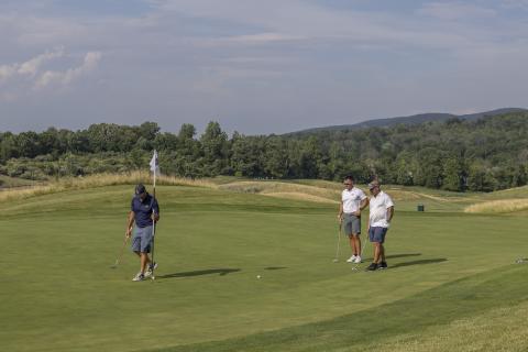 Golfers putting on Ballyowen Golf Course with mountains in background.