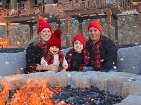 Family of four sitting around firepit during a snow storm.