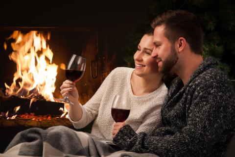 Couple sitting in front of fireplace drinking wine.