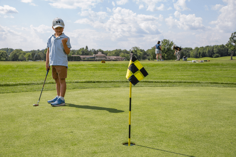 Child standing next to golf flag.