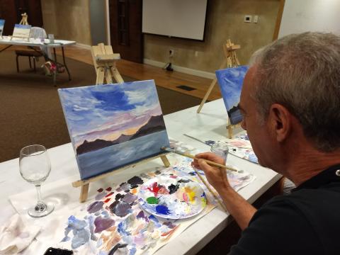 Person drinking wine and painting on canvas.