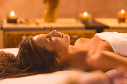 Woman laying in white towel on spa table surrounded by candles.