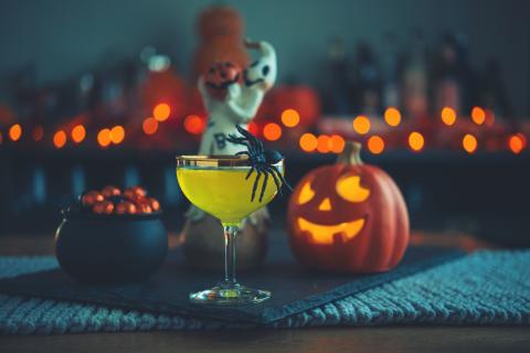 Yellow cocktail drink with fake spider hanging on side.