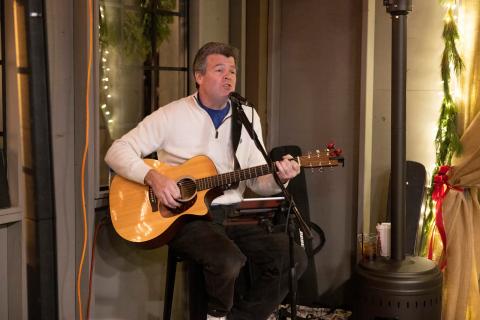 Man sitting on chair playing guitar and singing.