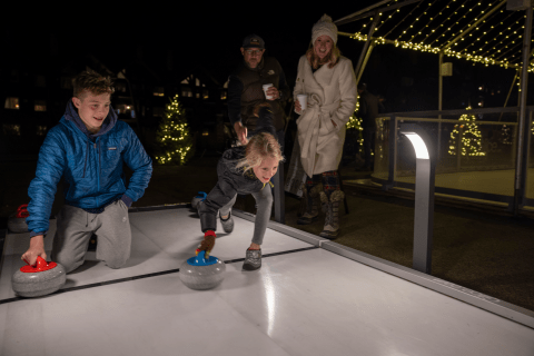 Boy and girl about to push curling stone down ice.