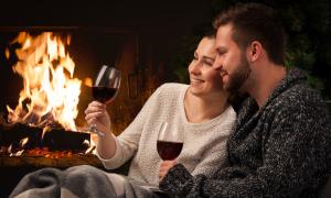 Couple sitting in front of fireplace drinking wine.