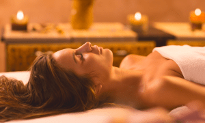Woman laying in white towel on spa table surrounded by candles.