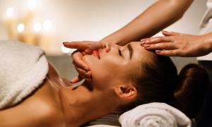 Woman laying on table with facialists hands on her chin and forehead. 