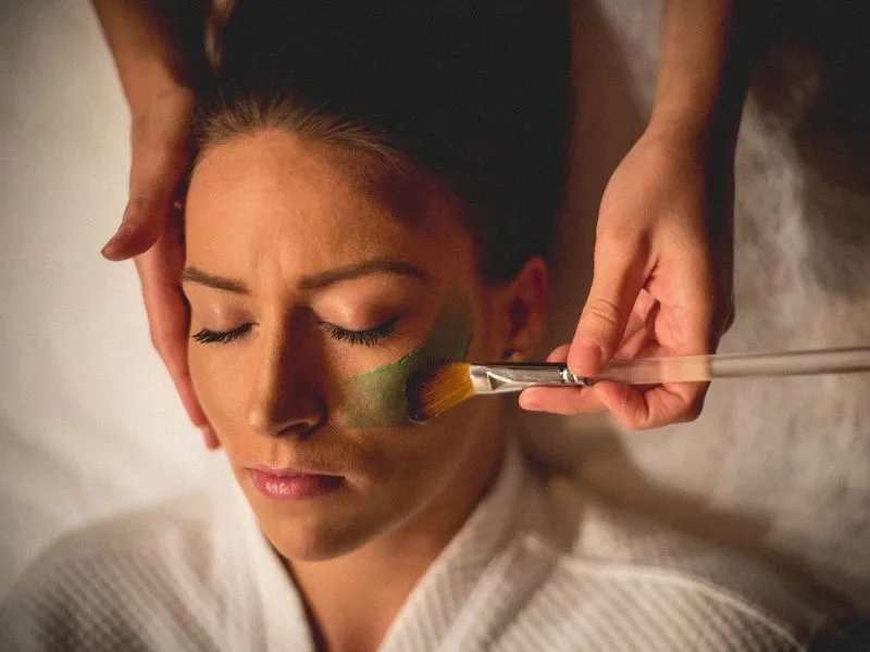 Facialist applying green face mask to woman's face.