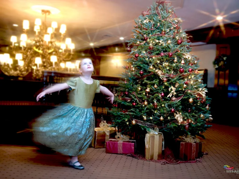 Little girl dancing by a Christmas tree. 