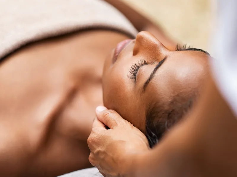 Woman laying down with tech's hands on side of her head for spa treatment.