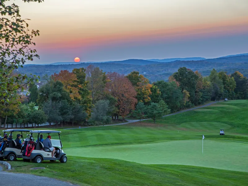 Two golf carts in front of a course during sunset