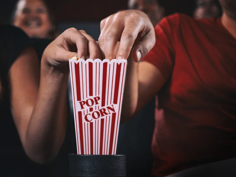 Two hands reaching in to popcorn holder.