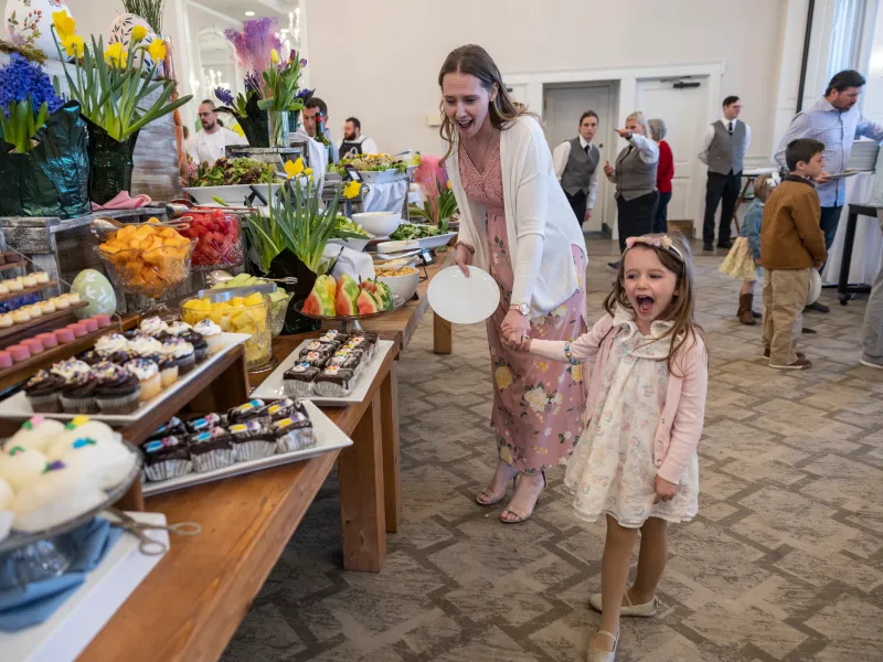Woman and child holding hands and looking at buffet of food. 